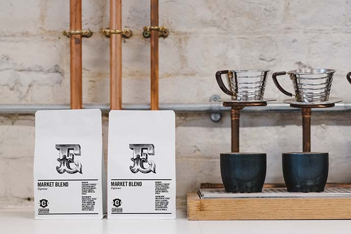 Coffee cups beside two Caravan coffee bags that read 'MARKET BLEND' each.
