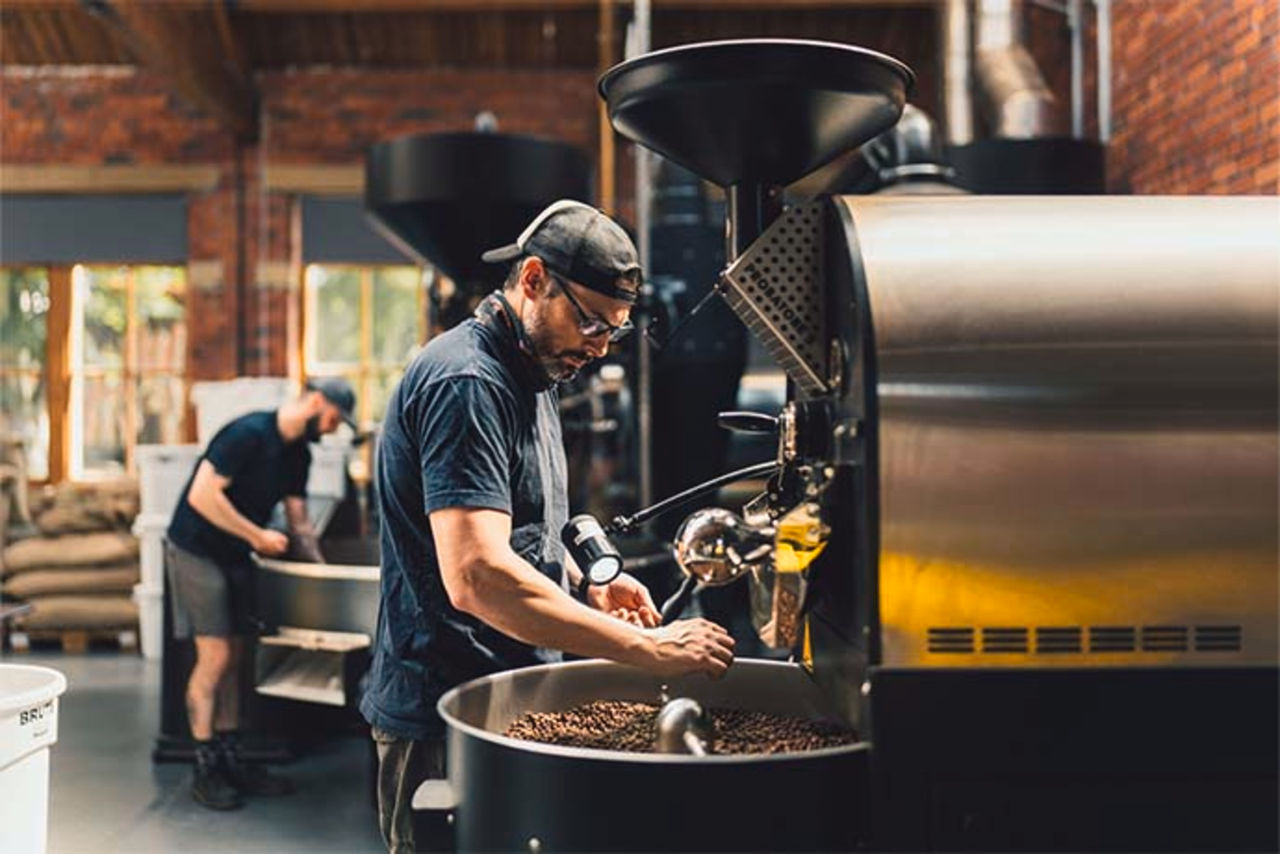 A staff member regulates a coffee roaster machine.