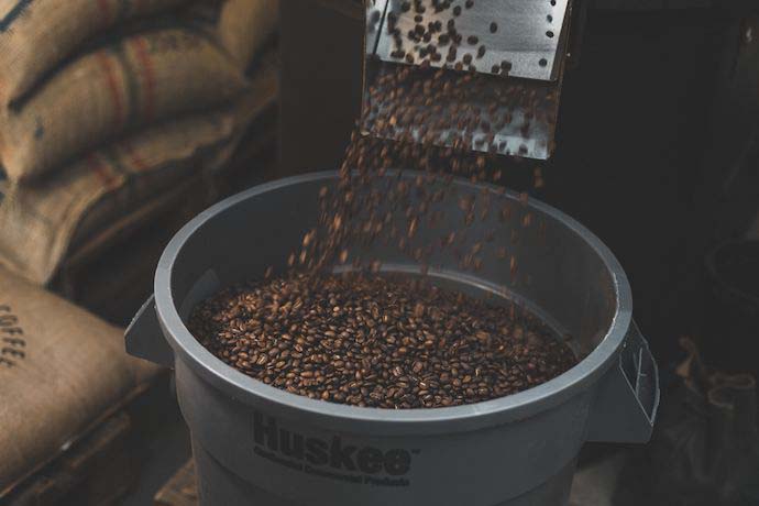 Coffee beans being poured into a bucket that reads 'Huskee'.