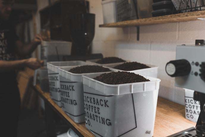 Coffee beans in buckets that read 'KICKBACK COFFEE ROASTING CO.' each. 