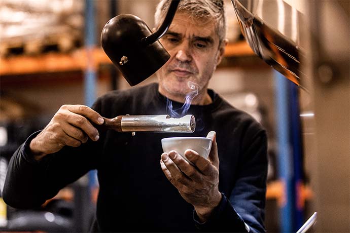 Man heating coffee beans using a cilindric tool and a cup. 