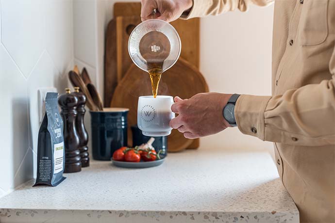 Coffee being poured into a cup in a kitchen environment.
