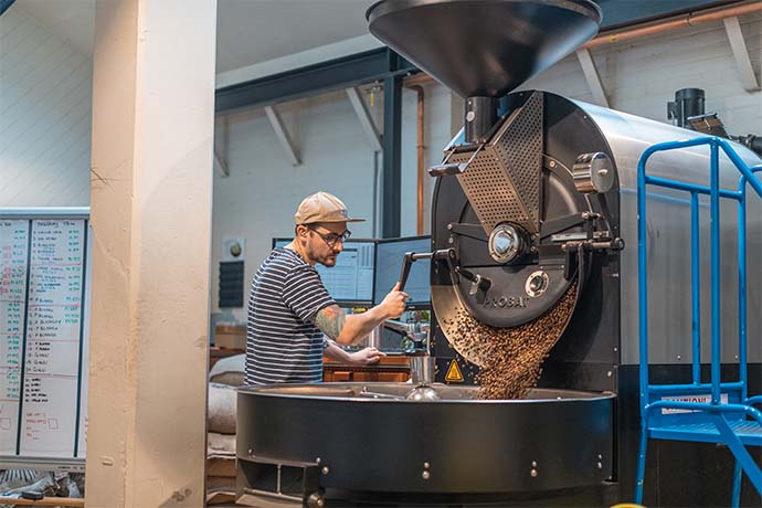 Workshop staff regulates a coffee roaster machine.