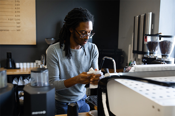 Barista standing in front of their coffee machine wiping their hand with a napkin.