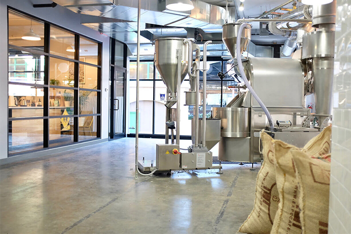 Bluestone Lane roasting location with their machinery and bags of green beans in foreground.