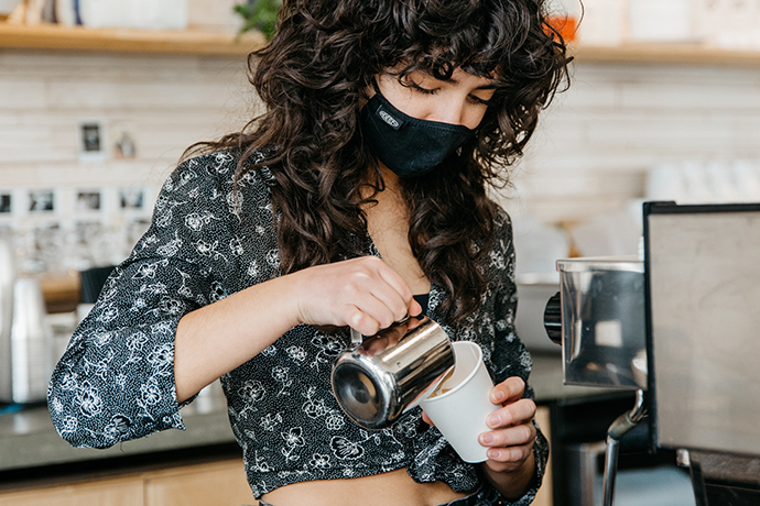 Coava barista pouring coffee into a paper cup.