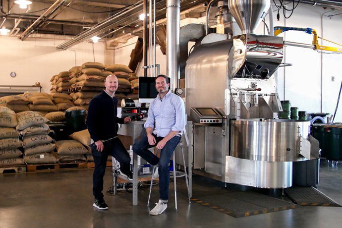 Coffee Manufactory staff with their roaster machine and burlap bags behind them.