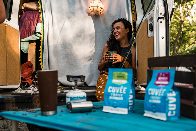 Cuvée coffee being enjoyed by a person in background whilst Cuvée coffee bags are displayed in foreground.
