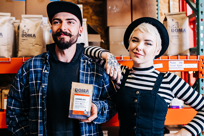 DOMA staff posing for a photo whilst staff on left holds a bag of DOMA coffee beans.