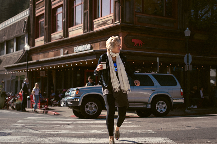Person crossing the road with their Equator branded coffee cup with an Equator cafe in the background.