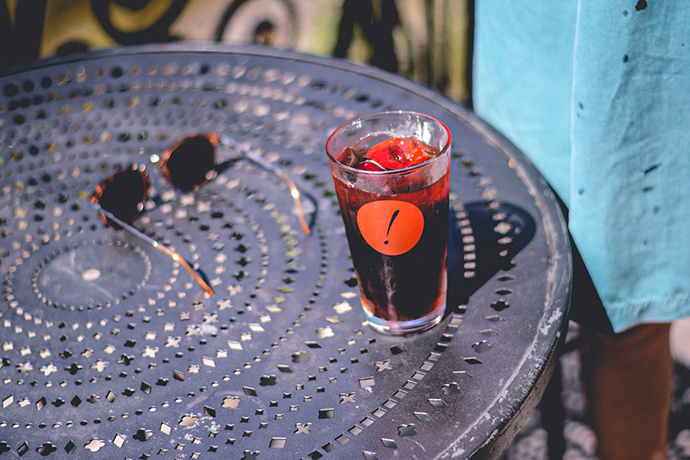 Gimme! Coffee glass filled with a dark red liquid next to a pair of sunglasses on an iron table.