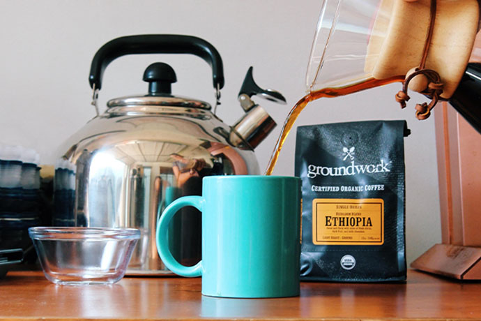 Coffee being poured from a flask into a mug with Groundwork Ethiopia coffee in background.