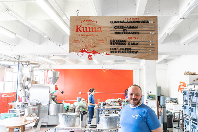 Kuma coffee roastery with roasting equipment and sign overhead.