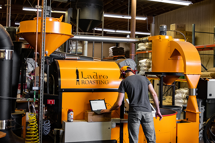 Ladro Roasting staff monitoring their yellow roaster machine with a laptop.