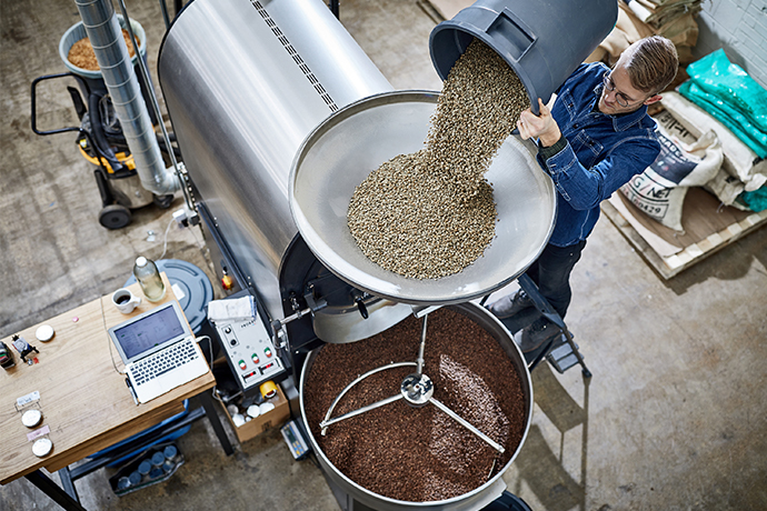 Roaster at Madcap loading coffee greens into a roaster machine.