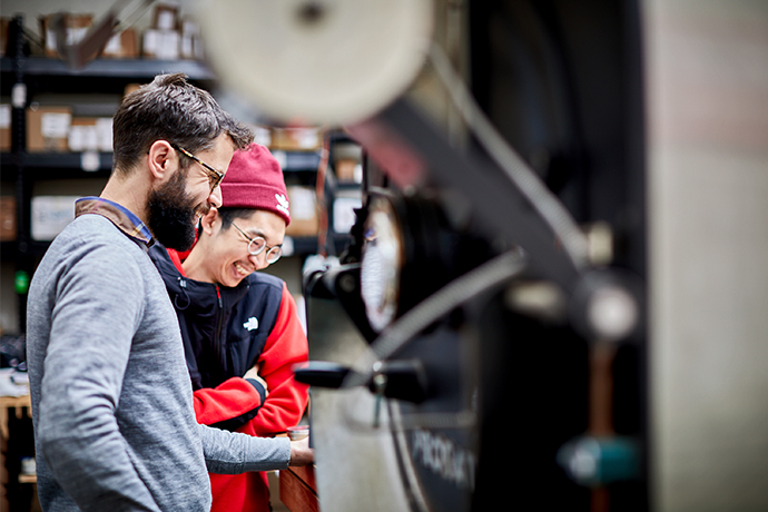 Visitors to Madcap roastery smiling in the background with machinery in foreground.