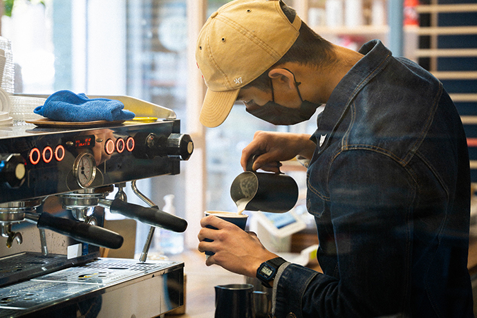 Barista at Metric pouring milk into a paper coffee cup.