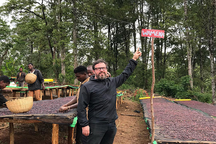 Person pointing at a sign that says 'Wamena' and smiling.