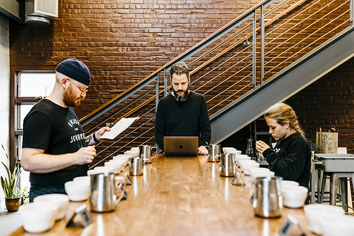 Three people comparing notes at cupping room at Passenger's cafe.