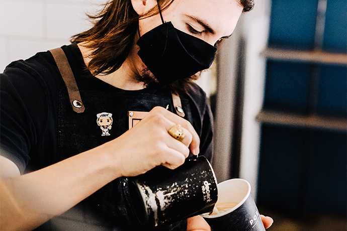 Portola barista pouring latte art into a paper cup.