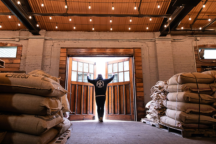 Person opening barn doors with burlap sacks of beans in the foreground.
