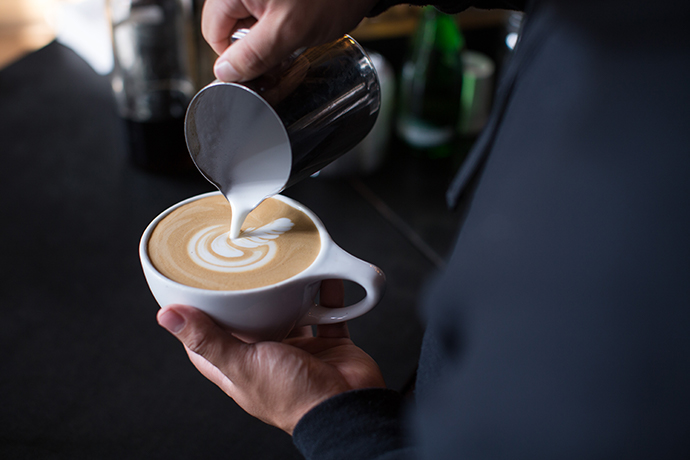 Barista pouring latte art into a coffee cup (finishing).