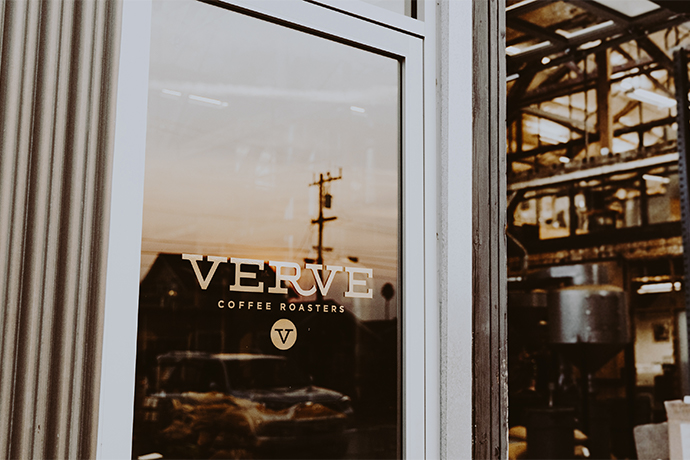 Door to Verve cafe with reflection of a sunset or sunrise visible on the glass door.