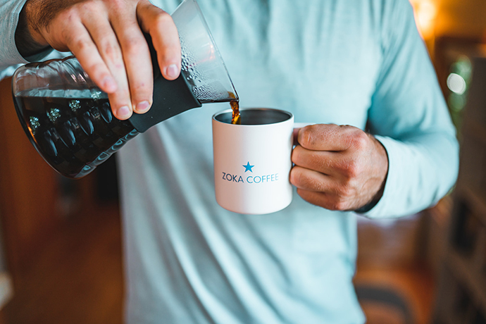 Coffee being poured from a flask into a Zoka Coffee branded mug.